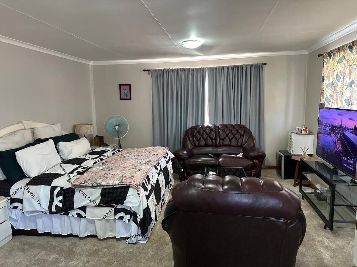 Une chambre à coucher avec un lit, un fauteuil en cuir, une table basse en verre, un téléviseur et une fenêtre avec des rideaux.