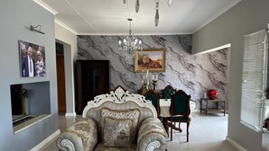 A spacious living room with a marble wall, a chandelier, a dining area with a table and chairs, and a sofa with decorative cushions.