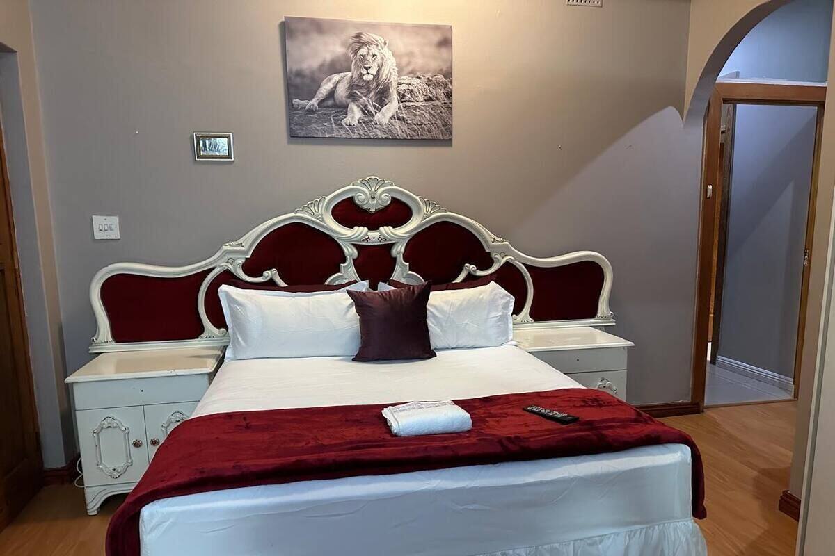Cama bem arrumada com manta vermelha, almofadas brancas e cabeceira branca.
