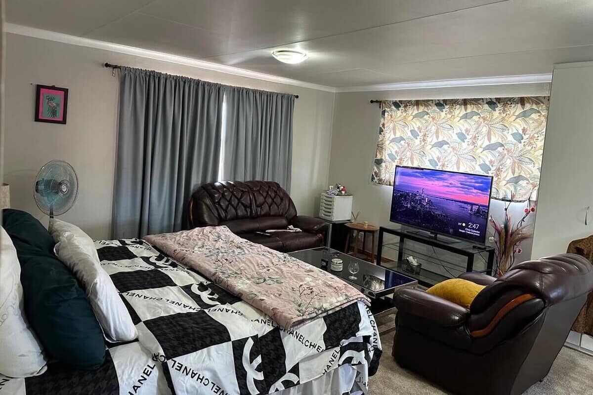 Uma sala de estar moderna com uma cama, um sofá de couro, uma televisão e uma janela com cortinas.