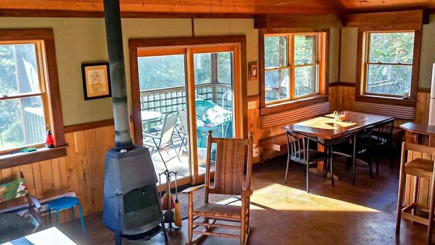 Un interior de cabaña acogedor, con una estufa de leña, una mesa de comedor y una silla.