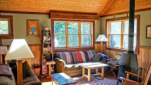 Un interior acogedor de cabaña con sofá, sillón, mesa y estufa de leña.