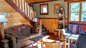 Un interior de madera con una escalera, un sofá, una mesa y una estantería.