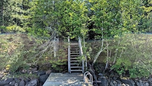 Una scala di legno conduce a un molo circondato da rocce e vegetazione lussureggiante.
