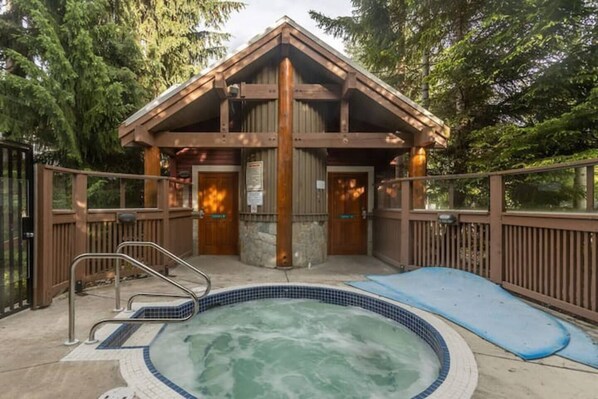 Escape to a secluded cabin surrounded by trees, featuring a hot tub and a cozy chimney.