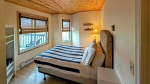 Un dormitorio con una cama, dos ventanas, un calefactor, una lámpara y techo de madera.