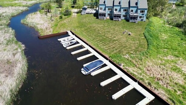 Una propiedad frente al río con un muelle, un edificio con varios balcones y una zona verde.