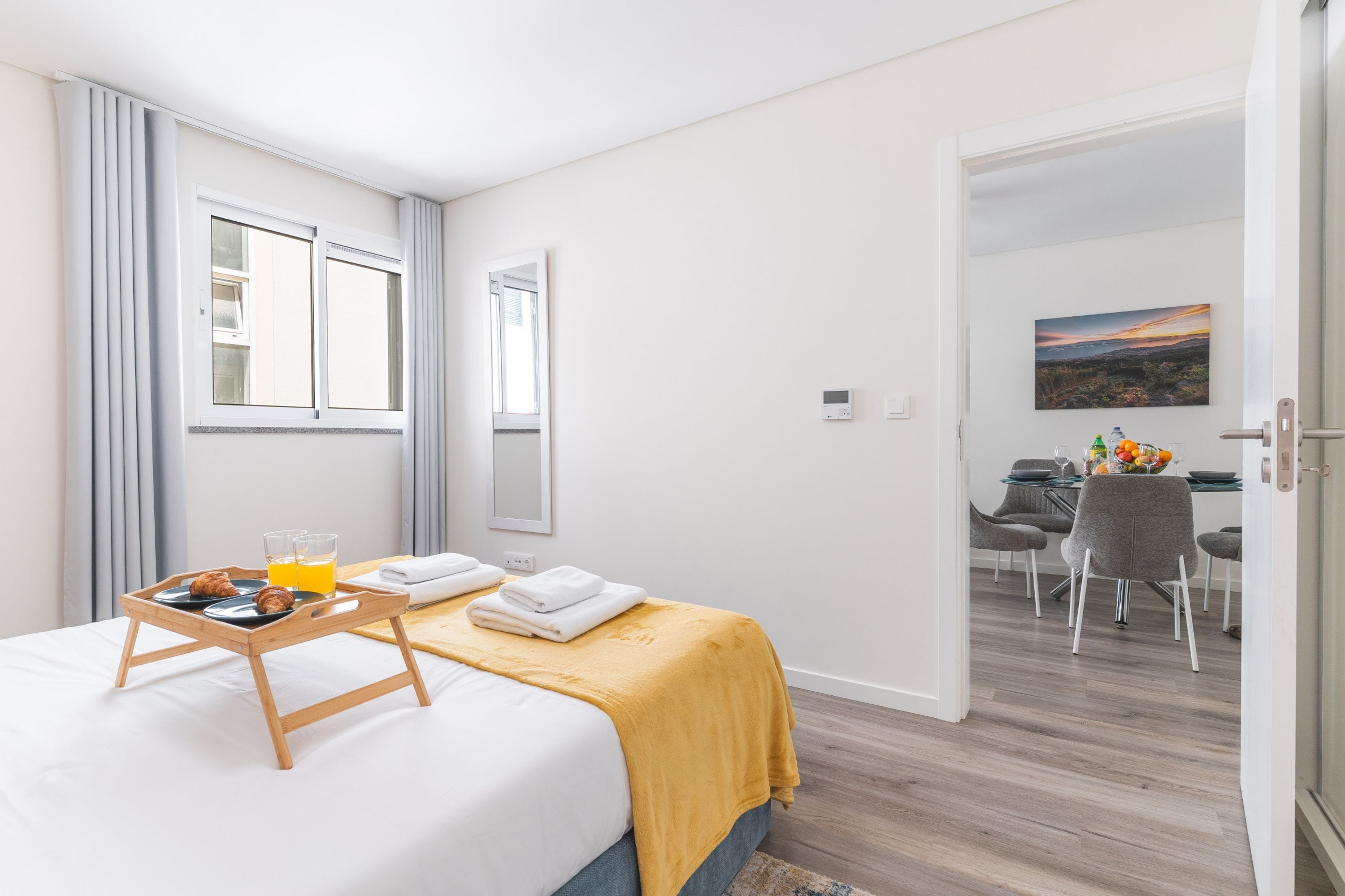A hotel room with a bed, breakfast tray, and a painting on the wall.