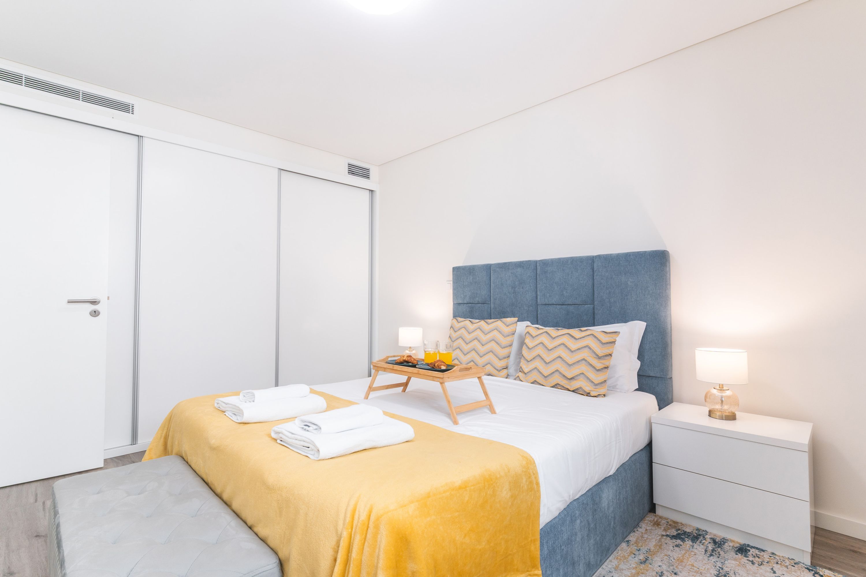 A hotel room with a bed, bedside tables, a bench, and a wardrobe.