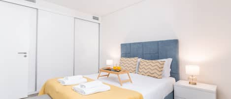 A hotel room with a bed, bedside tables, a bench, and a wardrobe.