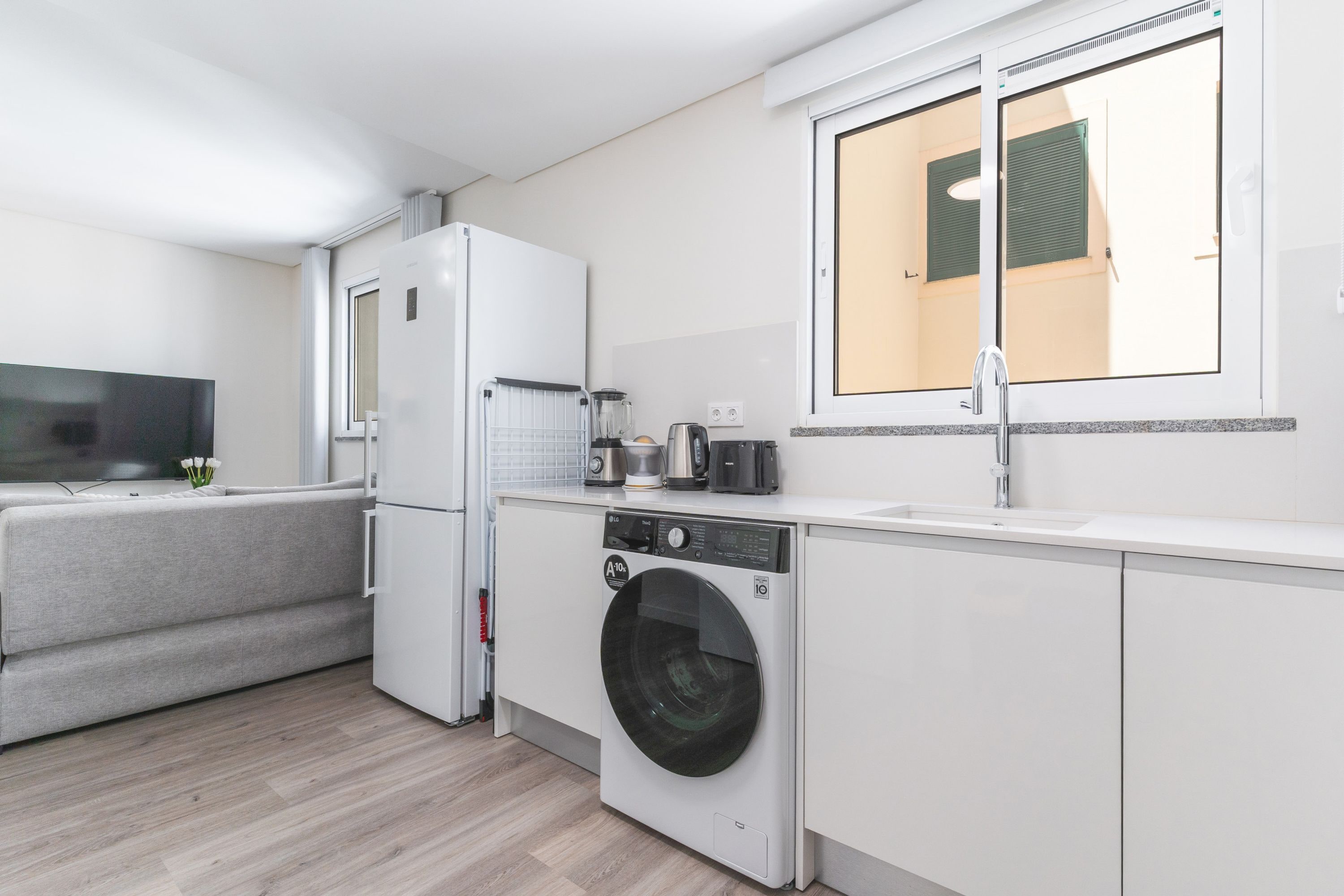 Cocina compacta con lavadora integrada, un pequeño comedor y ventana con persianas.