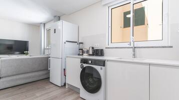 Cocina compacta con lavadora integrada, un pequeño comedor y ventana con persianas.