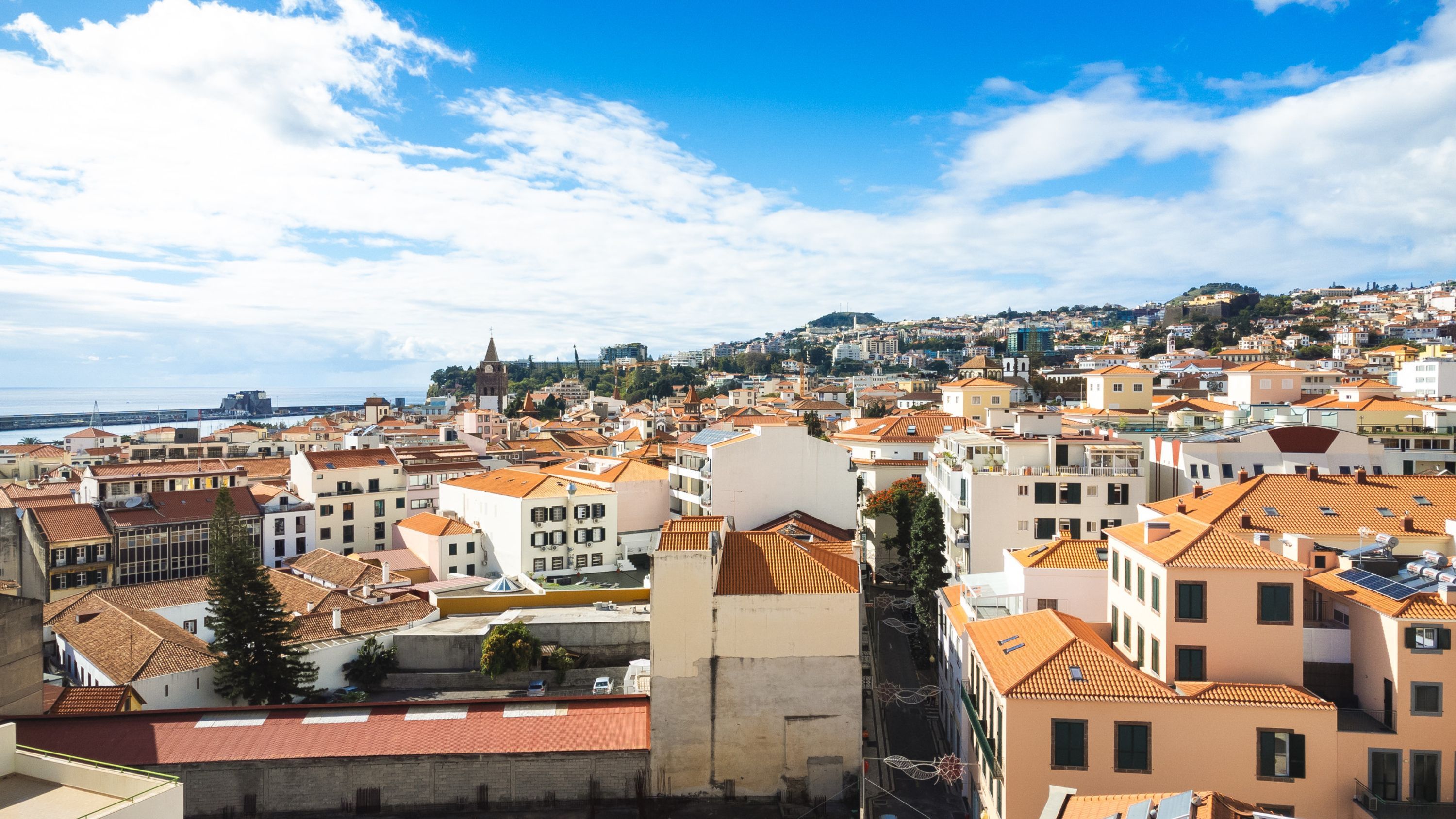 Paesaggio costiero con edifici a tetto in terracotta, un'imponente torre campanaria e vista sul mare.