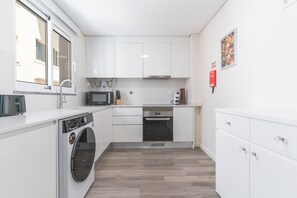 A compact kitchen with white cabinets, a microwave, an oven, and a washing machine. - Funchal Essence by Atlantic Holiday (Funchal)
