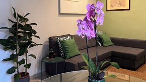 Ein modernes Wohnzimmer mit einem Glastisch, einer Couch und zwei Zimmerpflanzen.