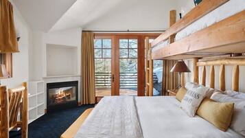 A bedroom with a large bed, wooden headboard, a fireplace, and a view through a glass door.
