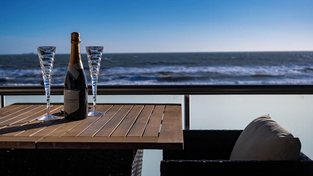 A bottle of Etimbeur champagne and two glasses on a wooden table with a view of the ocean. - Wight Stone Luxury Townhouse - Breathtaking Views  (Sandown)