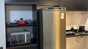 Eine kompakte Küche mit eingebauter Mikrowelle, einem Edelstahlkühlschrank und einem kleinen Regal mit einem roten Topf und einem Wasserkocher.
