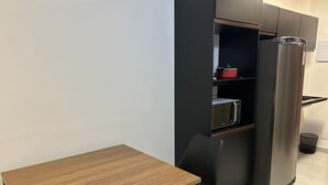 Eine kleine Küche mit einem Holztisch, einem schwarzen Stuhl, einer Mikrowelle und einem Edelstahlkühlschrank.