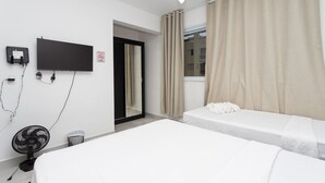 Een hotelkamer met twee bedden, een aan de muur bevestigde televisie, een plafondventilator en een raam met gordijnen.