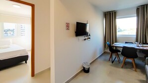 A hotel room with a bed, a TV mounted on the wall, a dining table with chairs, and a window with curtains.