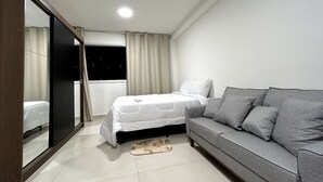 A modern bedroom with a bed, grey sofa, and a large mirror. - Studio 603 - proximo ao metro Santana - SP (São Paulo)