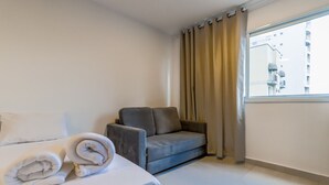 A hotel room with a bed, a grey armchair, and a window with curtains. - Studio 604 - Santana - proximo ao metro Santana (São Paulo)