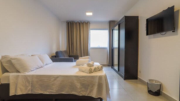 A hotel room with a bed, a sofa, a TV, and a window with curtains. - Studio 604 - Santana - proximo ao metro Santana (São Paulo)
