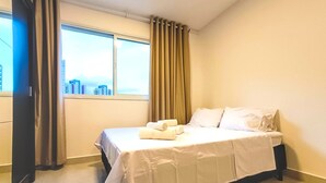 Ein Hotelzimmer mit Bett, einem Fenster mit Vorhängen und Blick auf Gebäude.