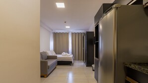 Une chambre d’hôtel moderne équipée d’une kitchenette, d’un canapé, d’un lit avec des serviettes pliées et d’une porte de salle de bain.