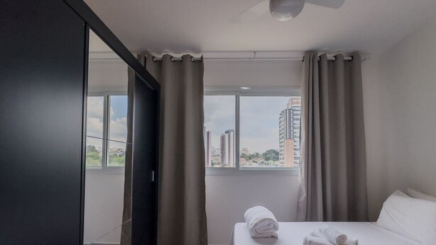 Ein Hotelzimmer mit Bett, Kleiderschrank, einem Fenster mit Vorhängen und Blick auf Gebäude.