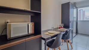 Eine moderne Küche mit Mikrowelle, Esstisch, Stühlen und Blick auf die Stadt durch ein großes Fenster.