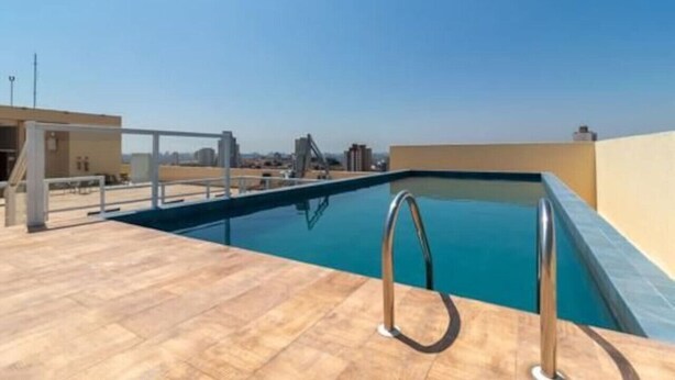 A rooftop swimming pool with clear blue water, a metal ladder, and a tiled deck. - Studio 612 - Tucuruvi - 20min do Anhembi (São Paulo)