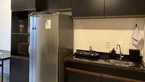 A modern kitchen with dark cabinetry, a stainless steel refrigerator, a sink, and a countertop. - Studio 612 - Tucuruvi - 20min do Anhembi (São Paulo)