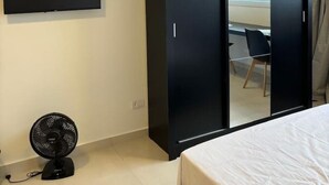 A hotel room with a bed, a TV mounted on the wall, a wardrobe, and a fan.