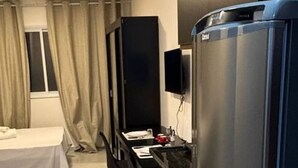 A compact hotel room with a bed, a desk, a chair, a TV, and a refrigerator. - Studio novo 405 - metrô Santana - sem Wi-Fi (São Paulo)