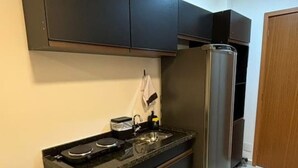 A modern kitchen with dark cabinets, a stainless steel refrigerator, and a black countertop. - Studio novo 405 - metrô Santana - sem Wi-Fi (São Paulo)