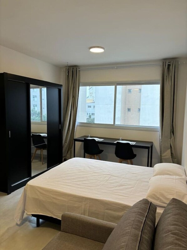 A bedroom with a bed, a desk, two chairs, and a wardrobe.