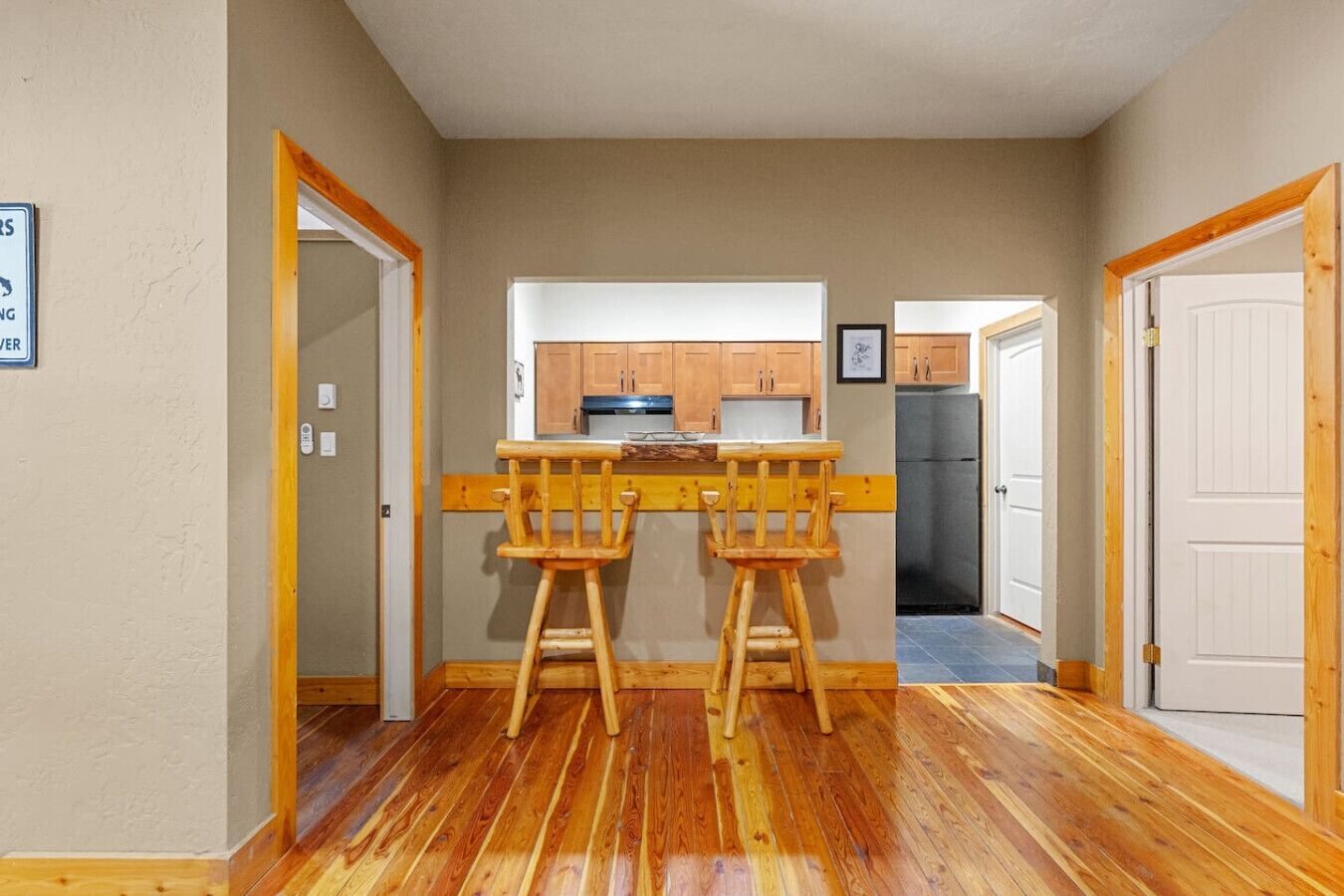 Une cuisine de taille réduite, avec des tabourets en bois, un réfrigérateur et des placards.