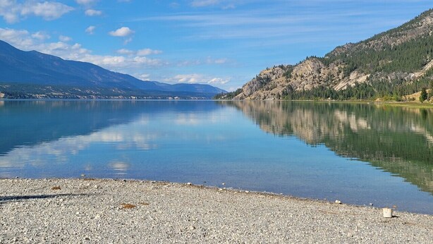 Un llac tranquil amb riba rocosa i muntanyes al fons.