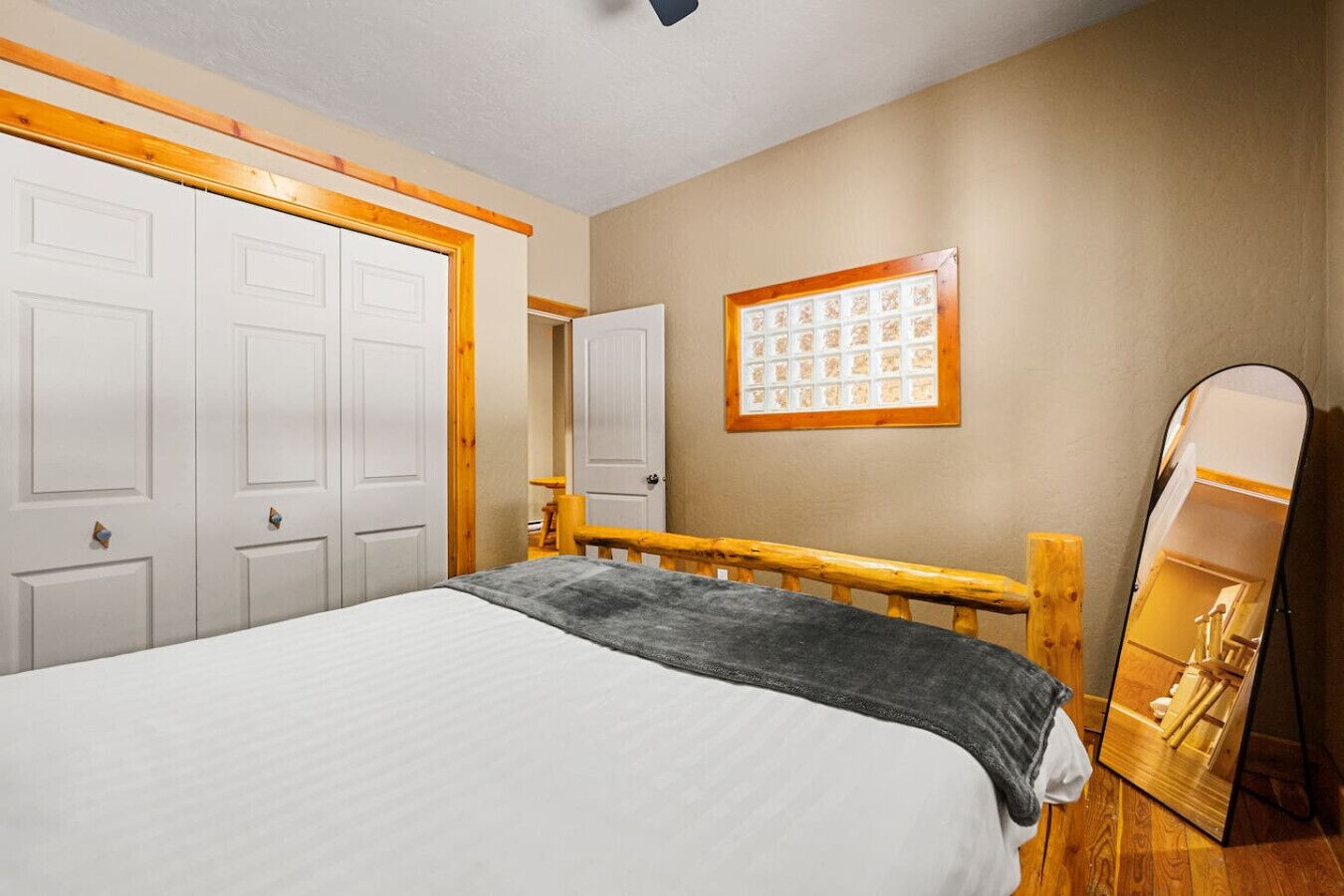 A bedroom with a bed, wooden headboard, white wardrobe, and a mirror.