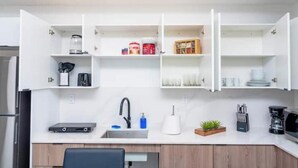 A compact kitchen with white cabinetry, a built-in sink, and a coffee machine.