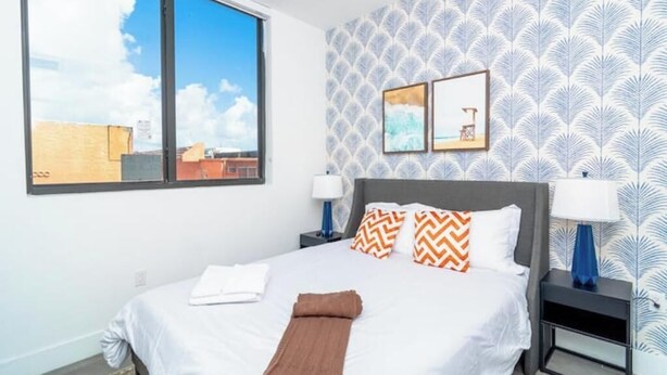 Quarto de hotel com uma cama grande, duas mesas de cabeceira, uma janela com vista para a cidade e papel de parede estampado.