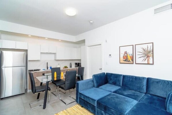 Een modern appartement met een kitchenette, een eethoek en een woonkamer met een blauwe bank.