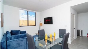 Uma sala de estar moderna com mesa de centro de vidro, sofá azul e TV fixada na parede.