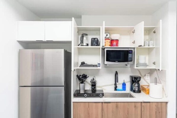 A compact kitchen with a stainless steel refrigerator, a microwave, and a coffee maker.