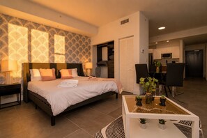 Una habitación de hotel moderna con una cama, mesitas de noche, un escritorio y un área de comedor.