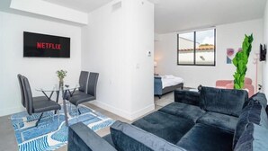 A modern living room with a black sofa, a glass coffee table, and a TV displaying "NETFLIX".