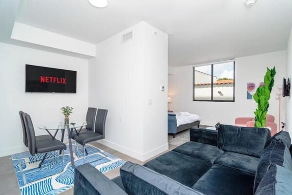A modern living room with a black sofa, a glass coffee table, and a TV displaying "NETFLIX". - King Bed brand new safe Oasis minutes to Brickell (Miami)