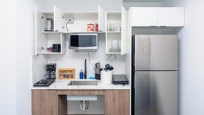 Une cuisine moderne avec des meubles blancs, un réfrigérateur en acier inoxydable, un four à micro-ondes et une machine à café.